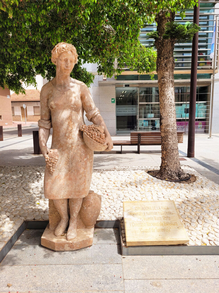 Staty av kvinna i klänning som skördar vindruvor.