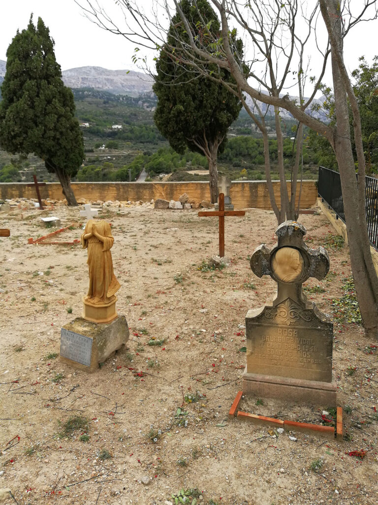 Kyrkogård med utspridda gravar, en med ett kors, en med en ängel utan huvud.