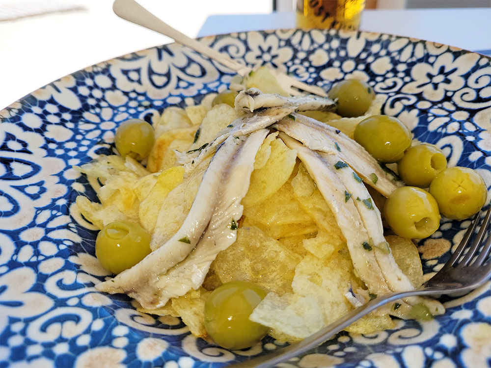 Tallrik med sardiner, oliver och chips.